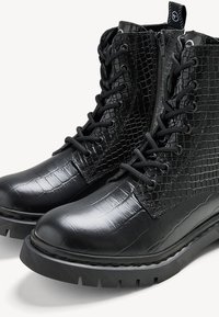 Bottines noires avec un motif en crocodile texturé, un laçage, une fermeture éclair sur le côté et une semelle en caoutchouc épaisse avec un profil cranté.