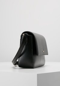 Black leather crossbody bag with a structured design, textured finish, flap closure, and an adjustable strap. Gold accent hardware present.