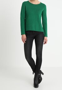Maglione verde a maniche lunghe in maglia con scollo rotondo, abbinato a jeans skinny neri a vita alta e stivaletti neri.