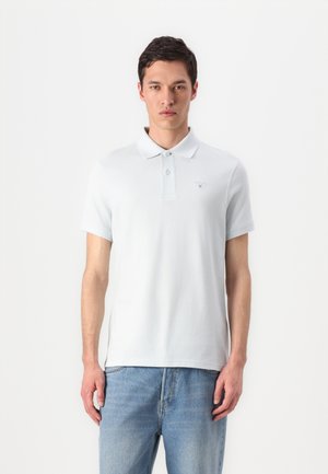 Lichtblauw poloshirt van katoen, met een kraag, drie knopen en een klein geborduurd logo op de linkerborst. Gekoeld met lichtblauwe denim jeans.