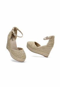 Espadrilles de cuña beige con un upper de tejido trenzado texturizado y tira en el tobillo. Presentan un tacón envuelto en yute y una suela plana y suave.