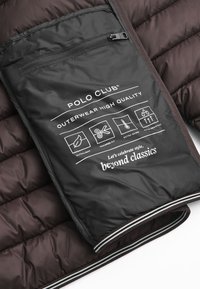 Mörkbrun vadderad ytterklädnad med en svart slitstark ficka som har vit text och ikoner. Inkluderar dragkedja och kontrasterande randigt kantband.