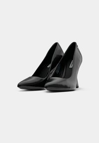 Pampoanele negre din piele lacuită cu toc înalt, având vârfuri ascuțite și un design structurat, caracterizate printr-o suprafață elegantă și netedă, cu o strălucire subtilă.
