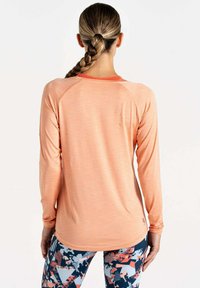 Langärmliges, hellorangefarbenes Sportshirt mit rundem Ausschnitt und Raglanärmeln. Kombiniert mit gemusterten blauen und orangefarbenen Leggings.