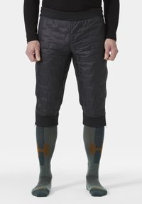 Czarne ocieplane spodenki z pikowaną fakturą oraz elastycznym czarnym paskiem w talii. Noszone z zielonymi skarpetkami do kolan posiadającymi geometryczne wzory i akcenty.