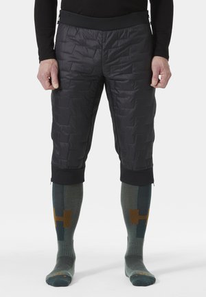 Zwarte gewatteerde geïsoleerde shorts met een elastische zwarte tailleband. Gemaakt met knielange groene sokken met geometrische patronen en accenten.