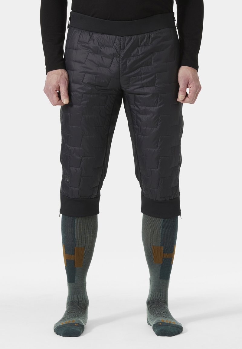 Czarne ocieplane spodenki z pikowaną fakturą oraz elastycznym czarnym paskiem w talii. Noszone z zielonymi skarpetkami do kolan posiadającymi geometryczne wzory i akcenty.