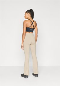 Μαύρο αθλητικό σουτιέν με σταυρωτό πίσω μέρος και μπεζ παντελόνι με φαρδύ κάτω μέρος, υφή υφάσματος λεία, ζώνη μέσης ψηλή, υπόδηση μαύρα παπούτσια τύπου slip-on.