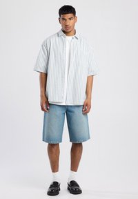 Blue and white striped short-sleeve shirt over a white T-shirt, paired with light denim shorts and black slip-on shoes. Bright, casual look.