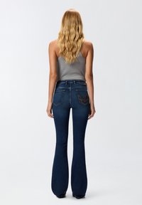 Modre široke jeans hlače z visokim pasom, ki imajo dve zadnji žepni z okrasnim šivanjem in gladko teksturo denima.