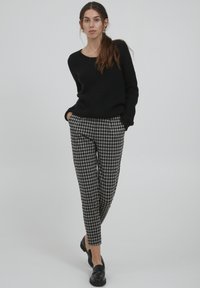 Černý žebrovaný svetr v kombinaci se šedými a černými kostkovanými kalhotami v slim fit střihu. Outfit doplňují černé mokasíny.