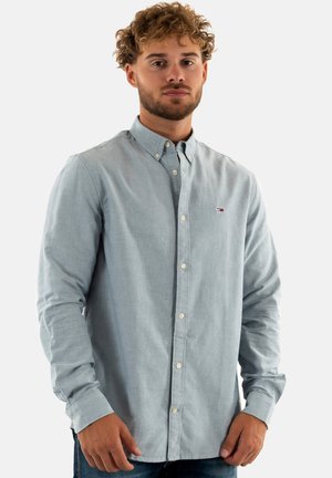 Camicia azzurro chiaro in tessuto morbido con colletto, bottoni bianchi e piccolo logo sul petto. Maniche lunghe incluse.