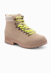 Botas de senderismo beige con cordones de neón amarillos, parte superior sintética texturizada, ojales de metal, cuello acolchado y suela de goma resistente.