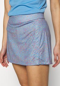 Modrá mini sukně s texturovaným vzorem drobných červených a žlutých teček. Má široký pasový pás pro pevné přilnutí. Hladká textura látky.