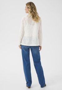 Witte kanten blouse met bloemenpatronen, lange mouwen en een losse pasvorm, gecombineerd met lichtblauwe, rechte jeans.