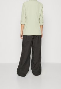 Světle zelené sako se tříčtvrtečními rukávy a klopovým límcem, spojené s volnými černými kalhotami z hladké, lehké látky.