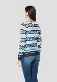 Kötött pulóver hullámos mintával, kék, krémszín és fekete árnyalataiban, lekerekített nyakkivágással és testhez simuló fazonnal.