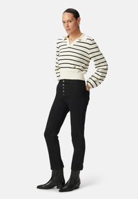 Pull en tricot rayé blanc et noir avec un col en V et des détails de boutons, associé à un jean noir taille haute avec un boutonnage à cinq boutons. Bottes noires à chevilles.