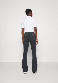 Μαύρα φουσκωτά τζιν με ψηλή μέση, πίσω τσέπες και ραφές αντίθεσης. Συνδυασμένα με ένα λευκό πουκάμισο με κοντό μανίκι. Εμφανίζονται από πίσω.