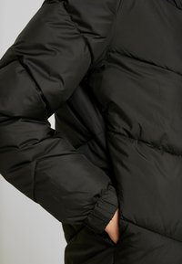 Svart puffjacka med kviltad design, elastiska ärmmuddar och en sidoficka. Materialet har en mjuk och lätt textur.