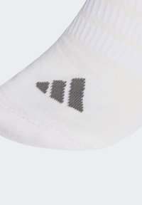 Calcetín blanco hecho de un material texturizado con rayas gris claro. Presenta un logo gris con tres rayas inclinadas cerca de la zona del dedo del pie.