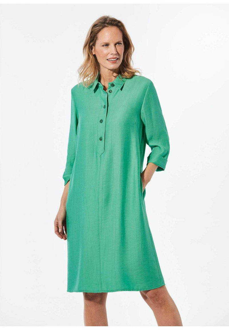 Grünes, knöpfbares Kleid mit Kragen, Dreiviertelärmeln und lockerer Passform. Hergestellt aus einem glatten, leichten Stoff mit einer dezenten Textur.