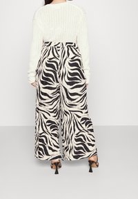 Vida byxor med ett svart och vitt zebramönster, med en plisserad textur. Bärs med en krämfärgad ribbad tröja och klackar.