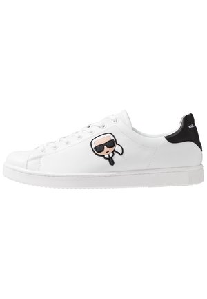 Hvid lavtop sneakers med sort hælflik og tegneserie ansigt med solbriller på siden, med snørelukning foran og flad sål.