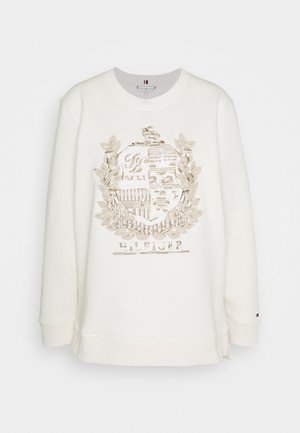 Sudadera de color crema con cuello redondo, que presenta un diseño de escudo bordado en tonos dorados y el texto "HILFIGER" en la parte inferior.