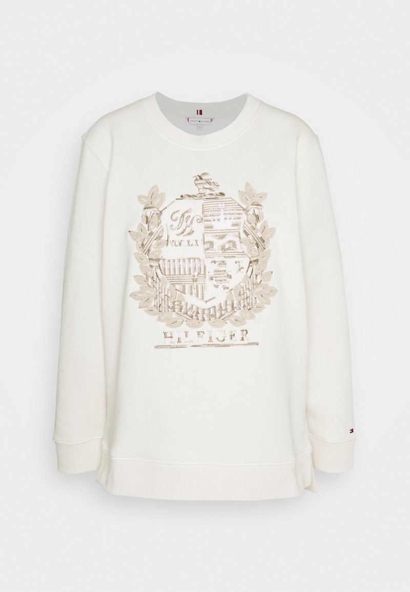 Sudadera de color crema con cuello redondo, que presenta un diseño de escudo bordado en tonos dorados y el texto "HILFIGER" en la parte inferior.