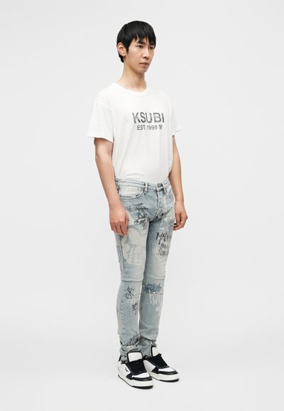 Valge lühikeste varrukatega T-särk, millel on tekst "KSUBI EST.1999". Tuimendatud sinised kulunud teksad graafiliste trükistega. Mustad ja valged kõrgete säärega tossud.