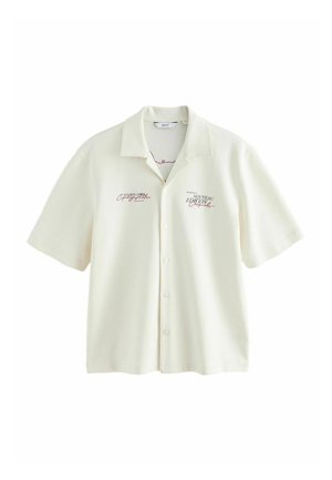 Krémová košeľa s krátkym rukávom na gombíky s golierom a červeným potlačeným textom na ľavej a pravej strane hrudníka.