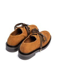 Chaussures en daim marron clair avec un bout arrondi, des lacets en ruban brun et une semelle plateforme noire épaisse. Elles présentent une texture lisse et des accents minimaux.