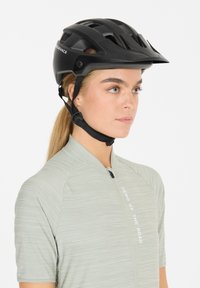Schwarzer Fahrradhelm mit Belüftungsöffnungen, verstellbarem Riemen und matter Oberfläche, getragen mit einem hellgrünen, strukturierten Shirt mit einem Frontreißverschluss.