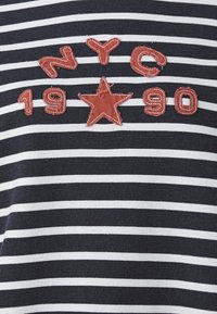T-shirt a righe blu navy e bianche con testo ricamato rosso "NYC 1990" e una stella. Tessuto in misto cotone con una consistenza liscia.