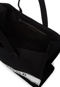 Fekete bevásárlótáska két fogantyúval, belső cipzáras zsebbel és fehér téglalap alakú címkével fekete szöveggel a külső oldalán.