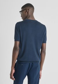 Maglione in maglia a maniche corte blu navy con colletto a costine e texture liscia, indossato con pantaloni coordinati dotati di due bottoni sulle tasche.