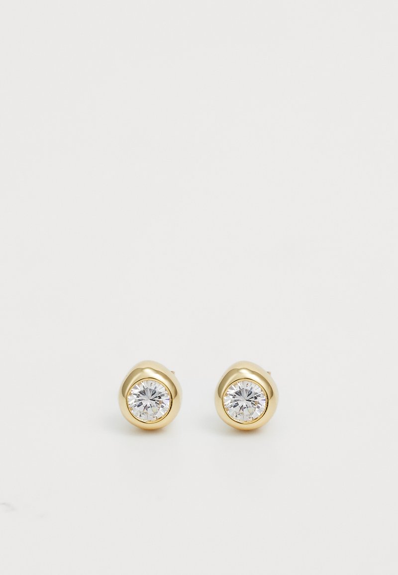 Brincos de studs em tom dourado com cristais transparentes redondos, apresentando uma parte de trás lisa e arredondada, com um design minimalista.