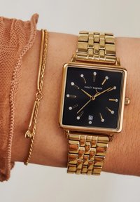 Gouden rechthoekige horloge met een zwarte wijzerplaat, diamantachtige uurmarkeringen, en een gouden metalen armband. Vergezeld van een dunne gouden kettingarmband.