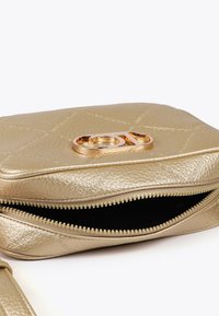 Borsa in pelle dorata con zip, superficie texturizzata e logo prominente sulla parte anteriore, parzialmente aperta per rivelare un interno scuro.
