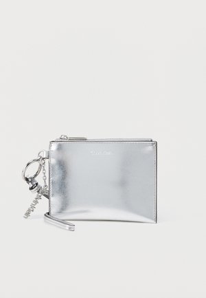 Zilverkleurige metalen Calvin Klein polstasje met ritssluiting en geëtste sleutelhanger op effen achtergrond.