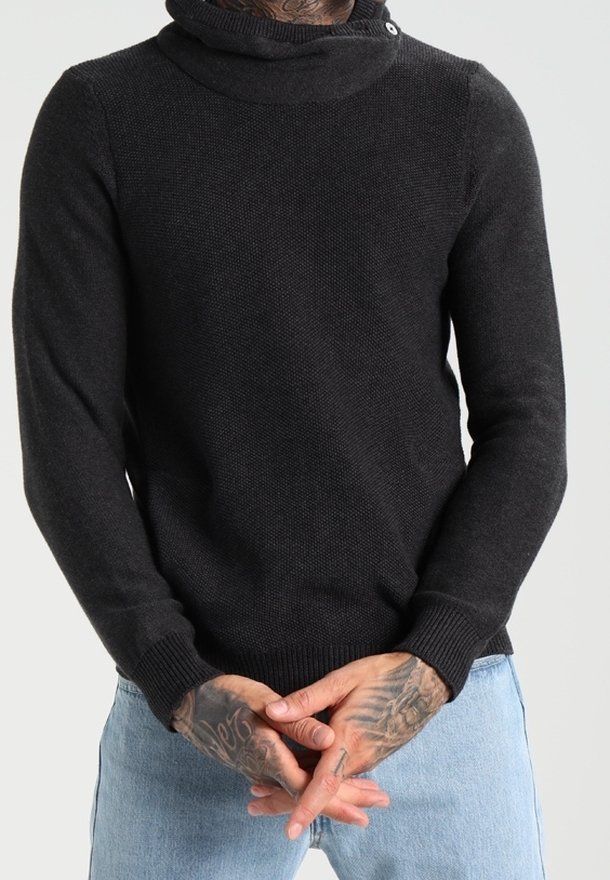 Pull en maille gris foncé avec col montant, manches longues, poignets côtelés et un détail bouton au niveau du col. Porté avec un jean bleu clair.