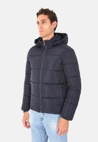 Giubbotto imbottito blu navy con zip frontale, cappuccio regolabile e design a righe orizzontali. Presenta tasche laterali e una texture di tessuto liscia.