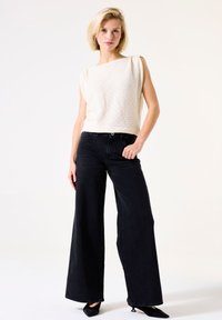 Witte textuur top met brede schouders, gecombineerd met hoge zwarte wijde jeans en zwarte puntige hakken.