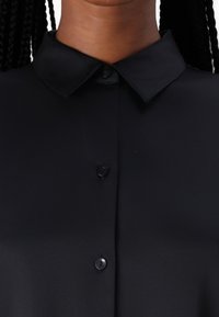 Svart skjorte med klassisk krage, som har en glatt tekstur og skjult knappeåpning, og som understreker et elegant, minimalisk design.