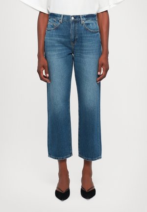 Woman wearing mid-rise, straight-leg blue jeans cropped above ankles, paired with black pointed-toe heels and a white top.