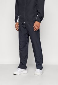 Marineblaue Windbreaker-Jacke mit weißen seitlichen Akzenten, kombiniert mit passenden marineblauen Hosen und weißen Sportschuhen. Leicht und mit glatter Textur.