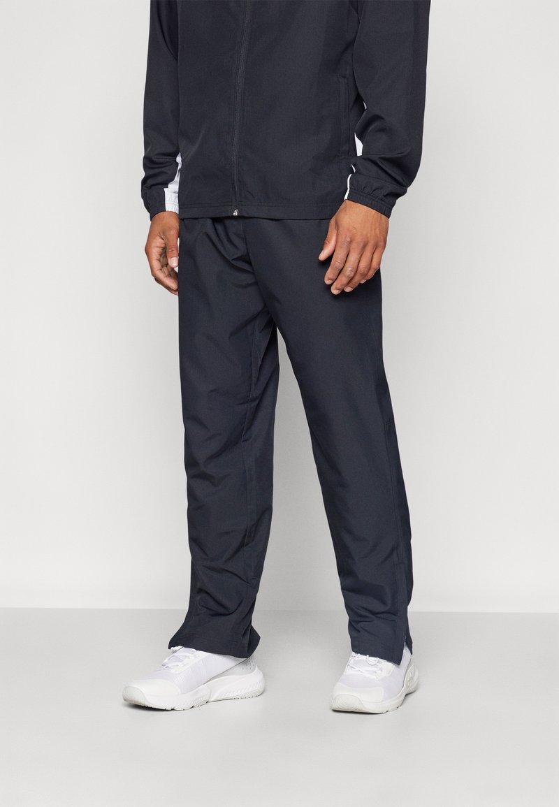 Marineblaue Windbreaker-Jacke mit weißen seitlichen Akzenten, kombiniert mit passenden marineblauen Hosen und weißen Sportschuhen. Leicht und mit glatter Textur.