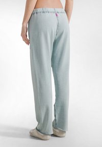 Pantalones azul claro de pierna ancha con cintura elástica, que presentan una pequeña etiqueta rosa. Tela suave con textura lisa y costuras laterales.