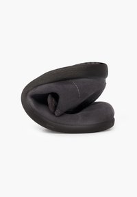 Zapatilla negra con una textura suave y aterciopelada. El diseño es abstracto, con una forma redondeada y un ligero pliegue en la tela.
